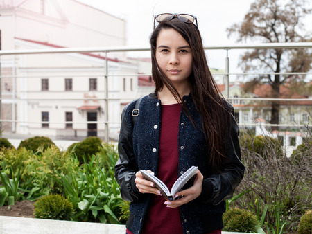 Young brunette woman standing outdoors, holding an opened book in the hands, street backgroundの写真素材