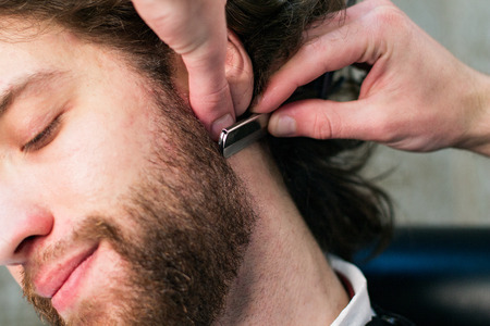 Close up man's face at the barber's - barber's hands are shaving his beard with a srtaight razor