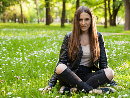 A young woman is sitting with crossed legs on the grass in the park and smilingの写真素材