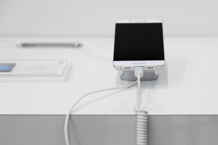 Close up mobile phone on a white showcase with  antitheft systemの写真素材