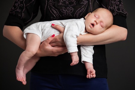 Woman's hands holding a newborn baby on the hands, baby is sleeping, gray backgroundの写真素材