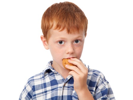 Close up a cute ginger boy eating a cookie, isolated on white background