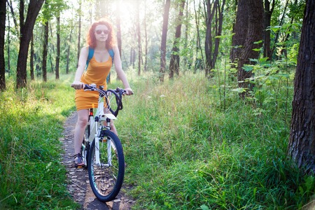 Young redhead woman in sunglasses riding a bike in in the forestの写真素材
