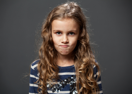 Portrait of a cute grimacing girl in a blue shirt, gray backgroundの写真素材