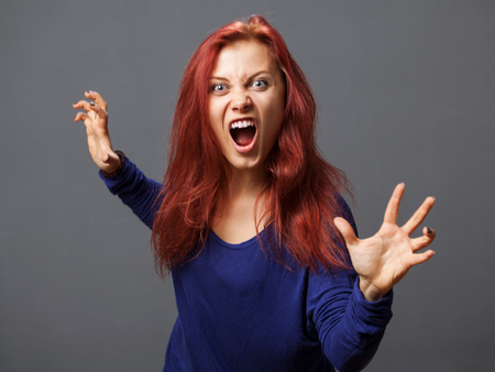 Young furious woman with opened mouth, gray backgroundの写真素材