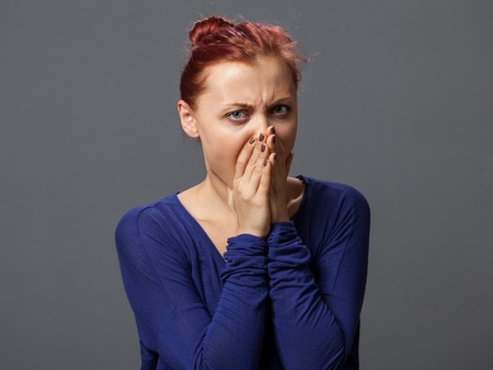 Young frightened woman, mouth is closed by the hands, gray backgroundの写真素材