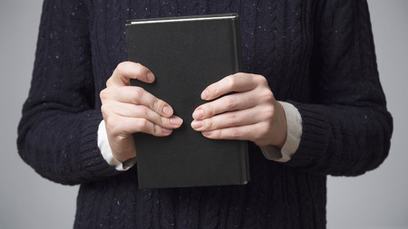 Woman's hands holding a black book, gray backgroundの写真素材