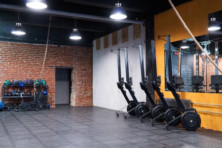 Modern fitness gym with a row of rowing machines and sport equipment at the wallの写真素材