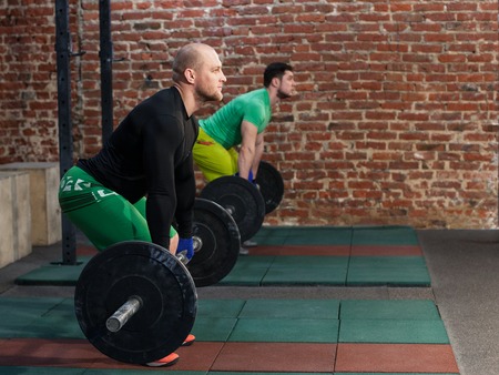 Two men are doing deadlift at the gym, red brick wall backgroundの写真素材