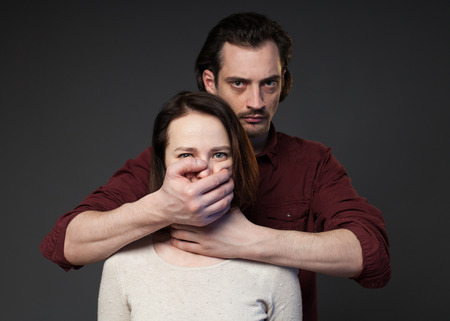 Family abuse - man closing womans mouse by the hand, gray backgroundの写真素材