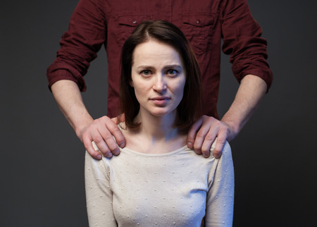 Family abuse - mans hands keeping womans shoulders, gray backgroundの写真素材