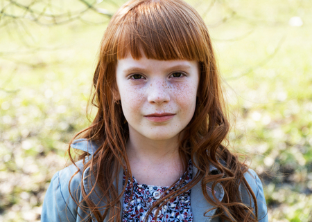 CLose up cute ginger girl with freckles against green fieldの写真素材