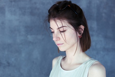 Beautiful sad girl lowered her eyes, portrait in profile, blue backgroundの写真素材