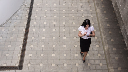Business woman walking on the sidewalk and using a smart phone, top viewの写真素材