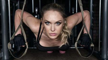 Fitness woman performs push-ups on suspension loops in the gymの写真素材