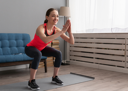 Happy fitness woman doing squat exercise at homeの写真素材