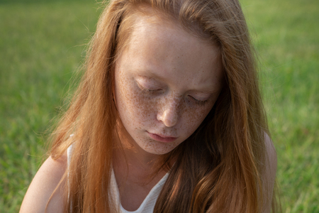 Gloomy face of sad little girl with freckles with lowered eyesの写真素材