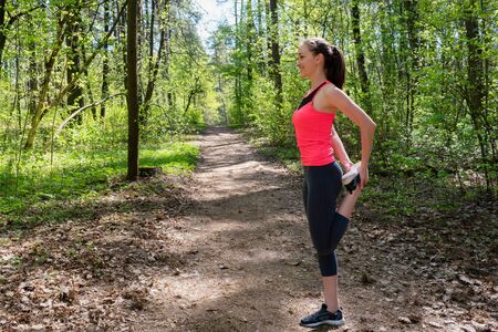 Fitness woman doing leg stretching before run in forestの写真素材