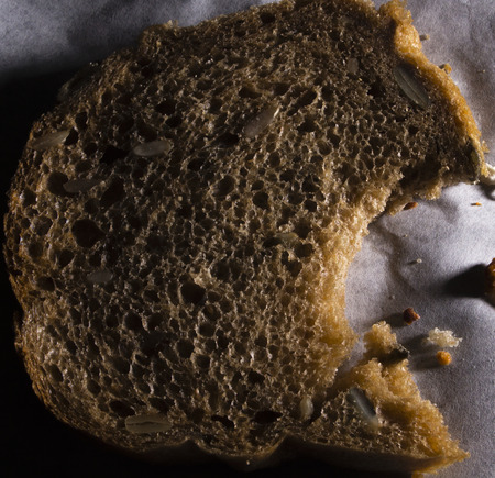 Slice of fresh bread little bitten with breadcrumbs aroundの写真素材