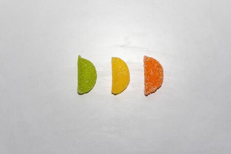 Three Sugar candies in a row. Green, yellow, orange. In a shape of half moon. Sorted in a row.の写真素材