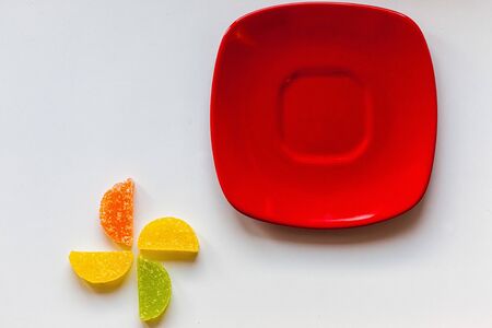 Four Sugar candies. Coloured green, yellow, orange. Shaped as half moon. One red plate.