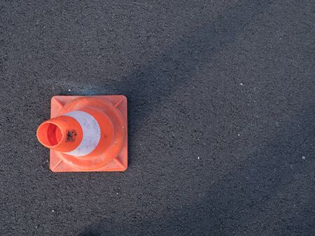 Traffic cone with shadow on asphalt. Traffic cone, with white and orange stripes on gray asphalt,...