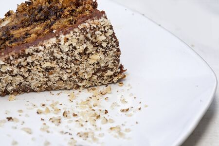 Close up view of a skice of brown, chocolate cake on a white plate. Chocolate crumbs can be seen on...