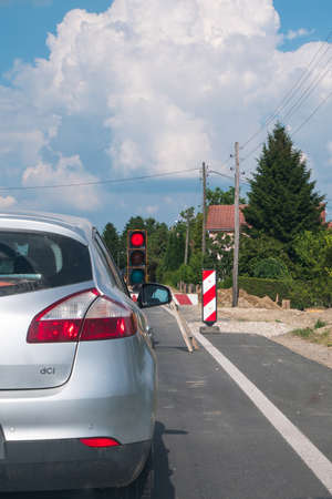 Road works in progress. The car is stopped in front of the road construction traffic light. The traffic light is red.の写真素材
