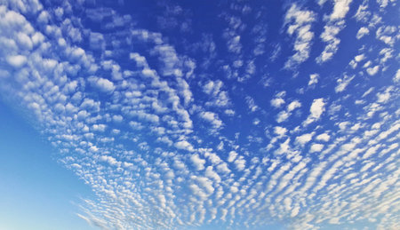 A stunning view of altocumulus clouds scattered across a vibrant blue sky at sunset. The soft,...