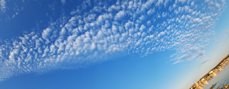 A picturesque coastal town at sunset with altocumulus clouds stretching across the blue sky. The...