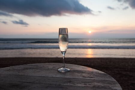 a glass of champagne or wine on the background of a beautiful sunset with clouds on the oceanの写真素材