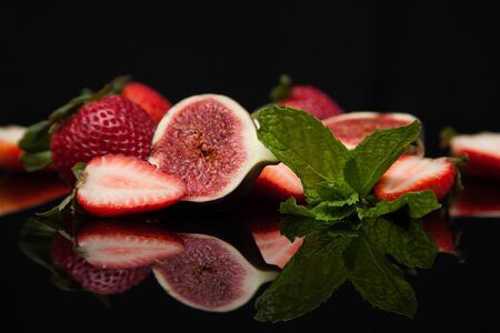 strawberries with figs and mint on a black background with reflection