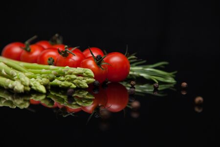 asparagus with tomatoes on a mirrored black tableの写真素材