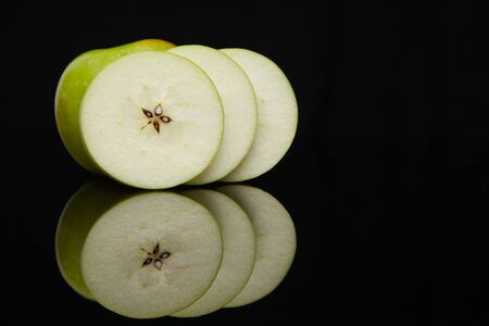 green apple slices on a black background with reflectionの写真素材