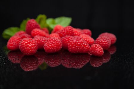 raspberries with mint leaves reflected on a black mirror tableの写真素材