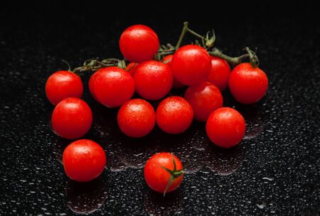 cherry tomatoes with drops on a black table with reflectionの写真素材