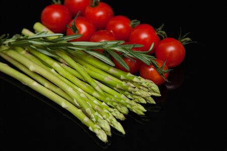 asparagus with tomatoes on a mirrored black tableの写真素材