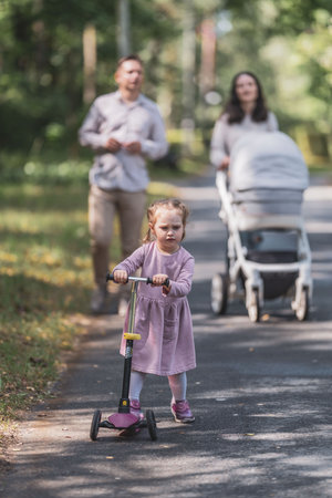 young mother and her little daughter riding scooter together in the parkの写真素材
