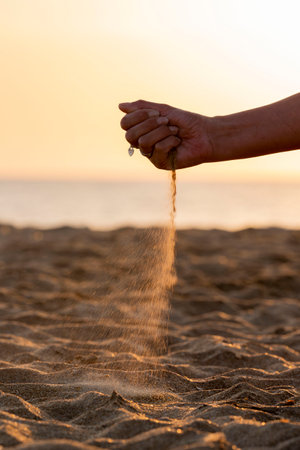 Closeup of a man's hand sprinkling sand on the beachの写真素材