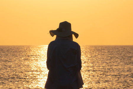 Silhouette of a woman in a hat at sunset on the beachの写真素材