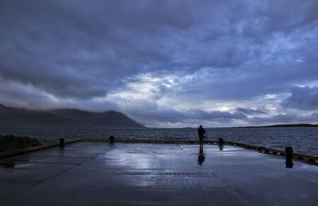 A person standing at Gledivik Bay looking at the dramatic stormy sky ahead, Djupivogur Village,...