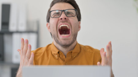 Close Up of Young Man with Laptop Shouting in Office, Failureの写真素材