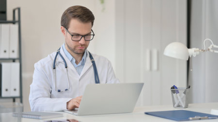 Male Doctor Working on Laptop in Officeの写真素材
