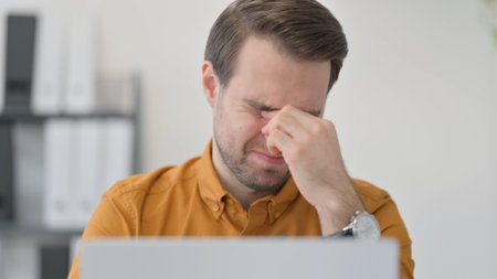 Close Up of Young Man with Laptop having Headache in Officeの写真素材