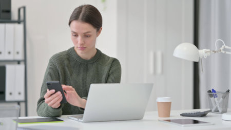Young Woman with Laptop using Smartphoneの写真素材