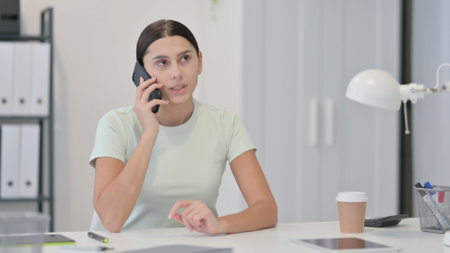 Young Latin Woman Talking on Phone at Workの写真素材