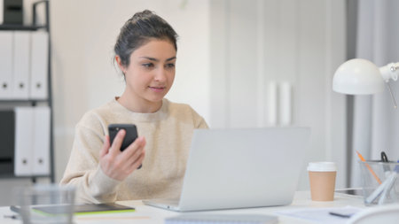 Young Indian Woman with Laptop using Smartphoneの写真素材