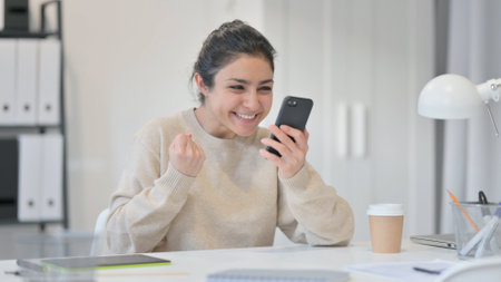 Young Indian Woman with Smartphone Celebrating Successの写真素材
