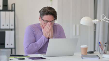 Middle Aged Man with Laptop Sneezing in Officeの写真素材