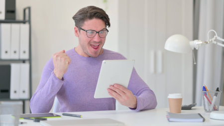 Middle Aged Man Celebrating Success on Tabletの写真素材